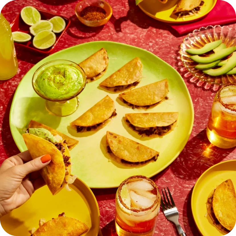 A colourful collage of a dinner table with a red table cloth and a plate of crispy tacos and a bowl of avocado cream